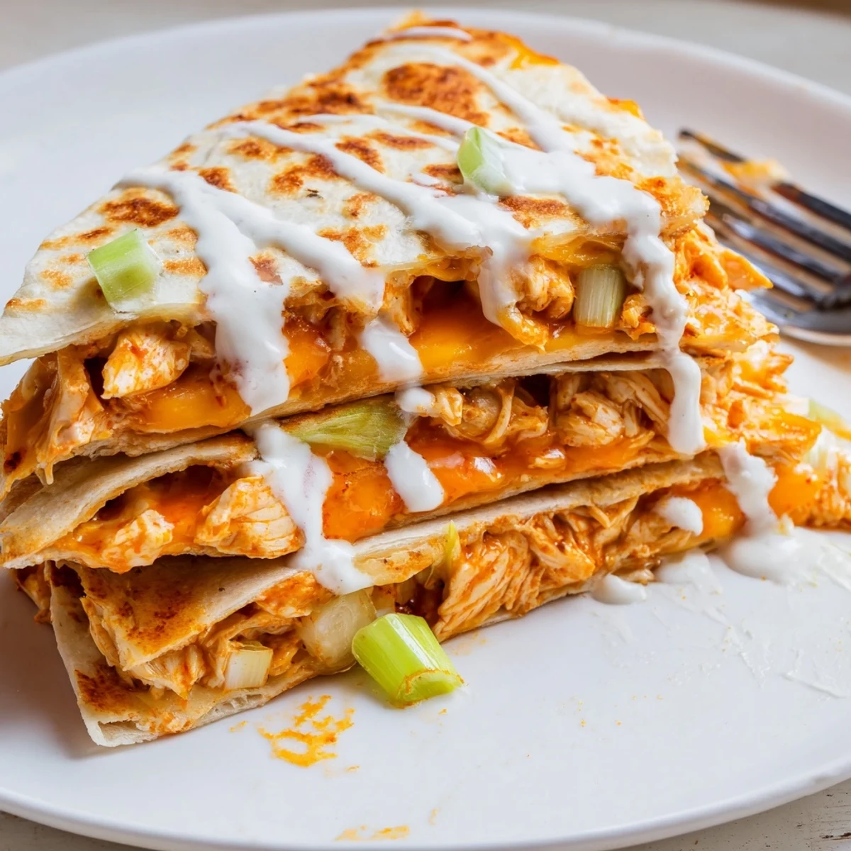Golden crispy Buffalo Chicken Quesadillas sliced into wedges with white ranch drizzle