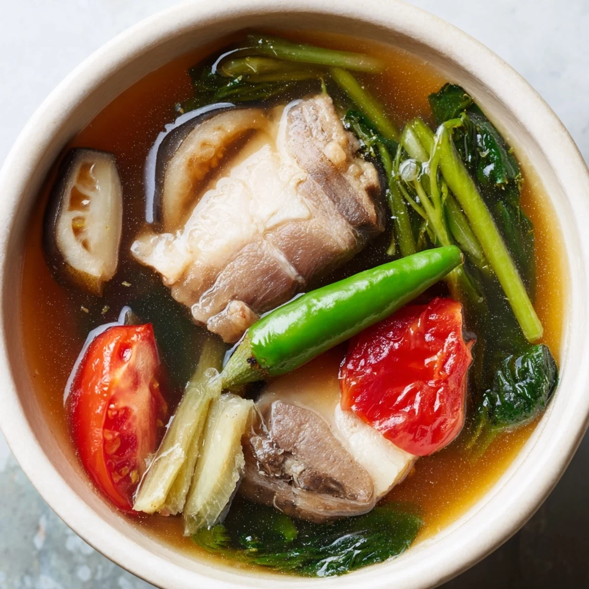 Bowl of Filipino Sinigang sour soup with tender pork and fresh vegetables steaming hot