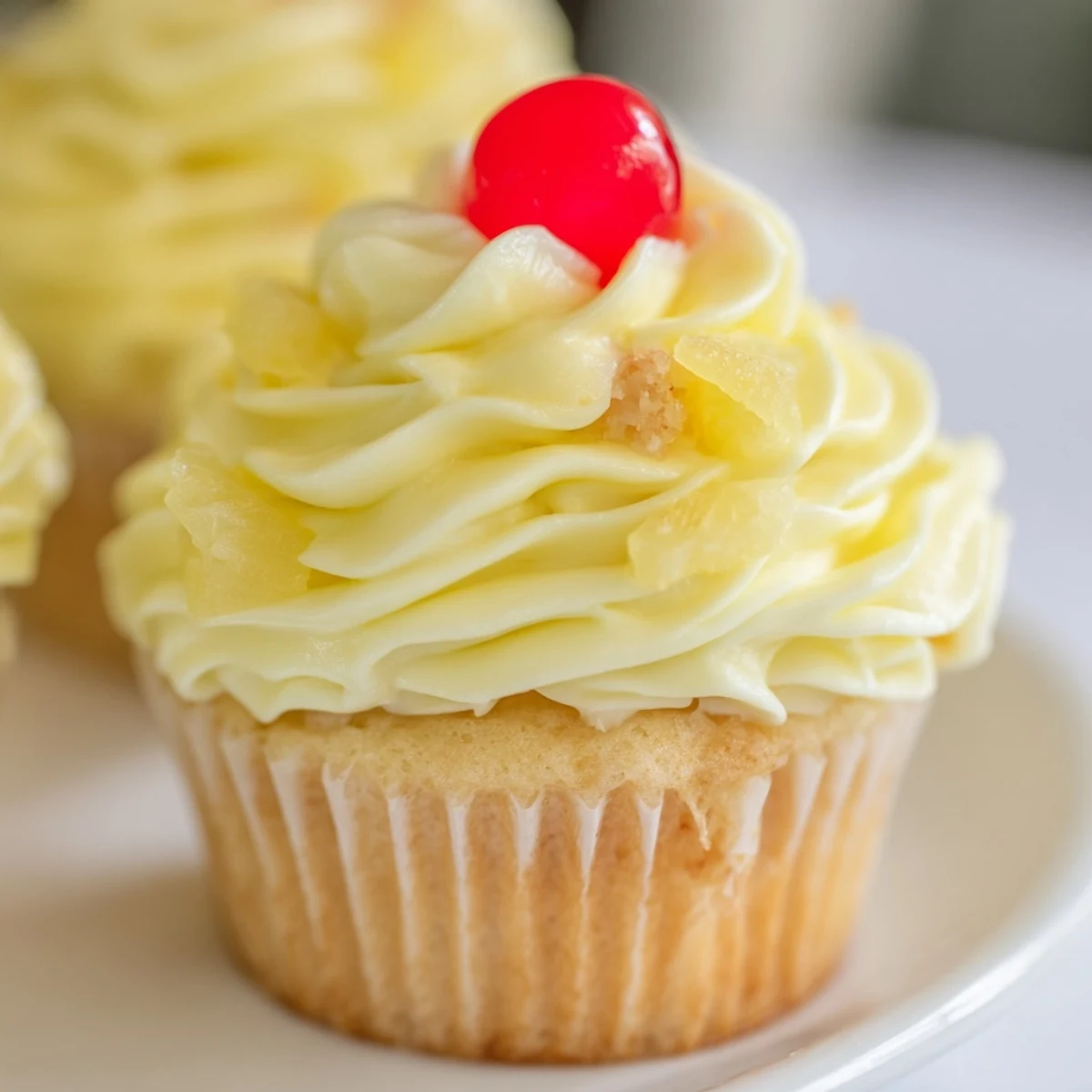 Golden Dole Whip Cupcakes topped with creamy pineapple frosting and a cherry