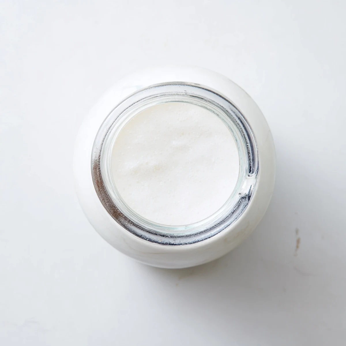 Homemade coconut milk poured into a glass jar with creamy white texture visible