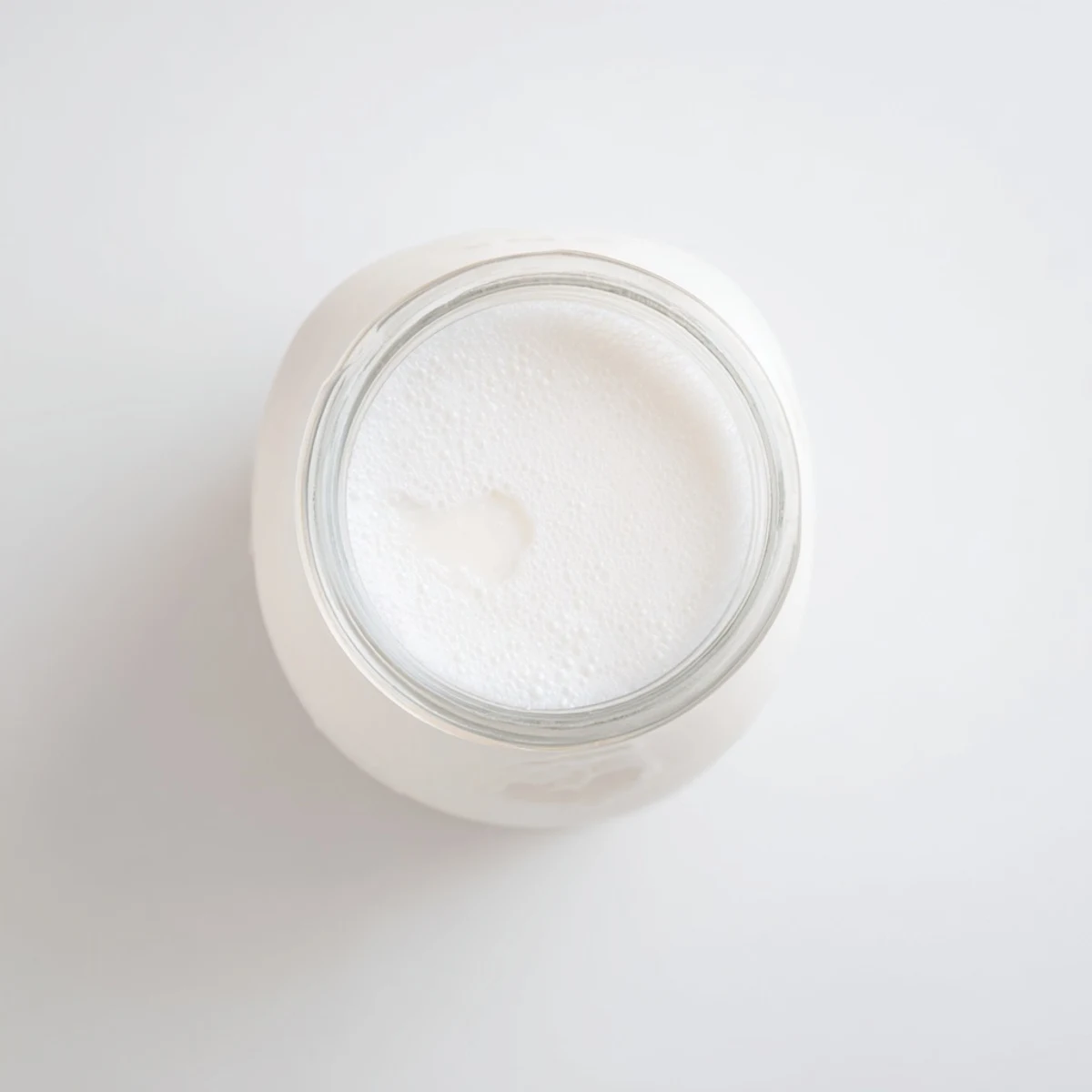 Glass of thick homemade coconut milk topped with coconut flakes on wooden table