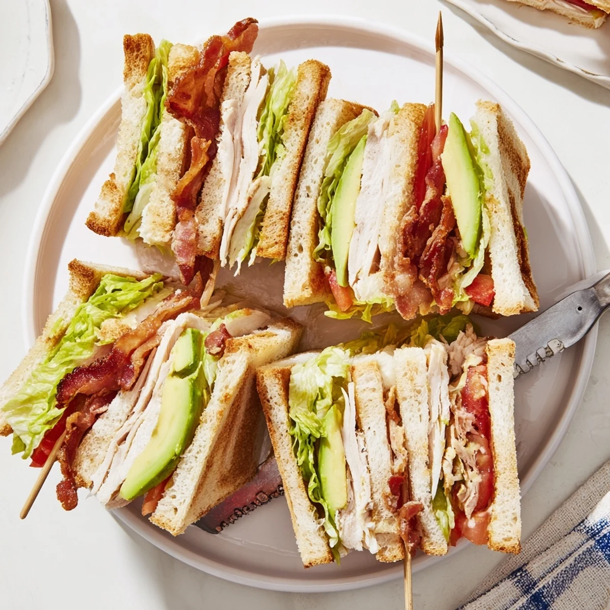 Stacked California Club Sandwich featuring roasted turkey, crispy bacon, creamy avocado slices, and fresh vegetables between three toasted layers