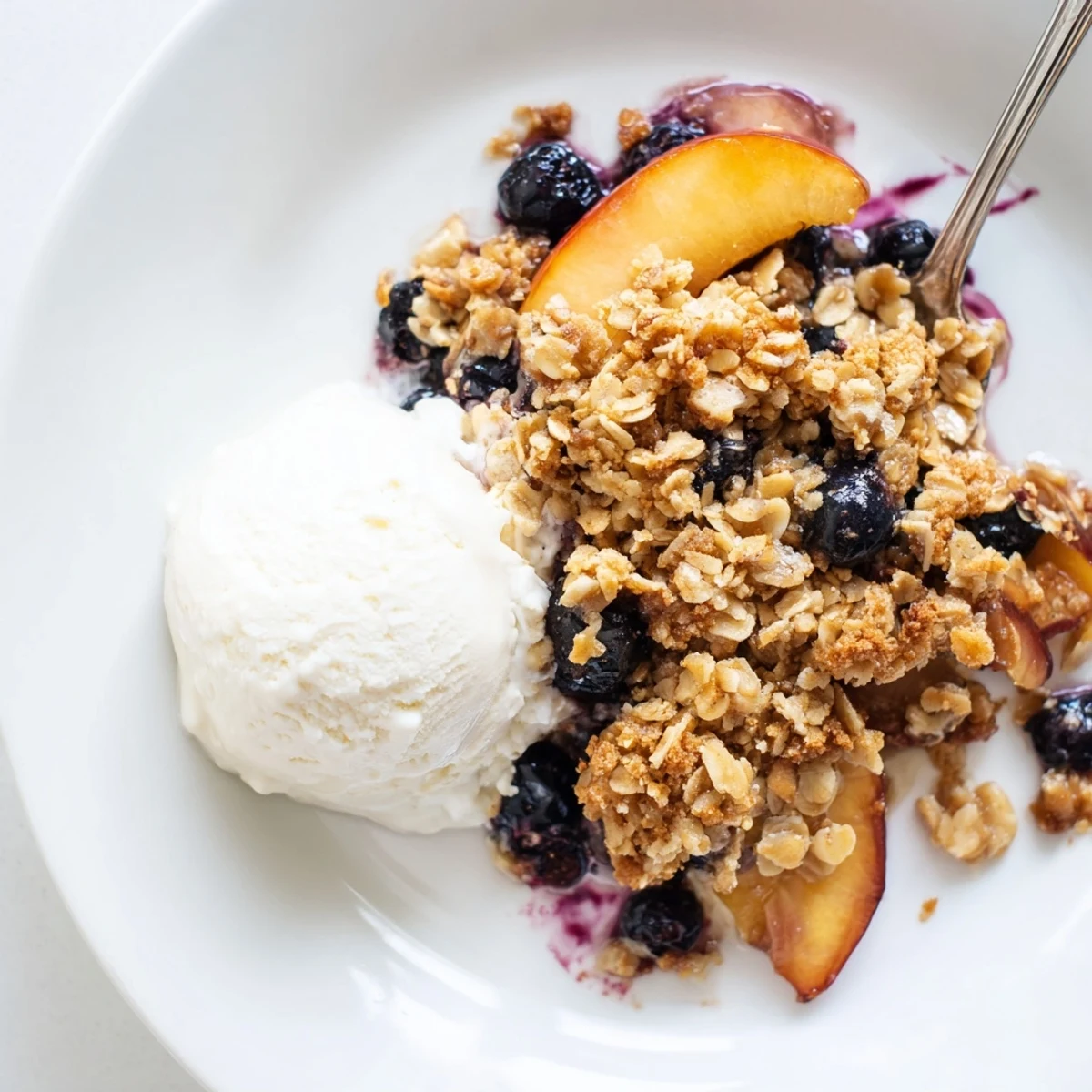 Warm Blueberry Peach Crumble spooned into a bowl with melting vanilla ice cream