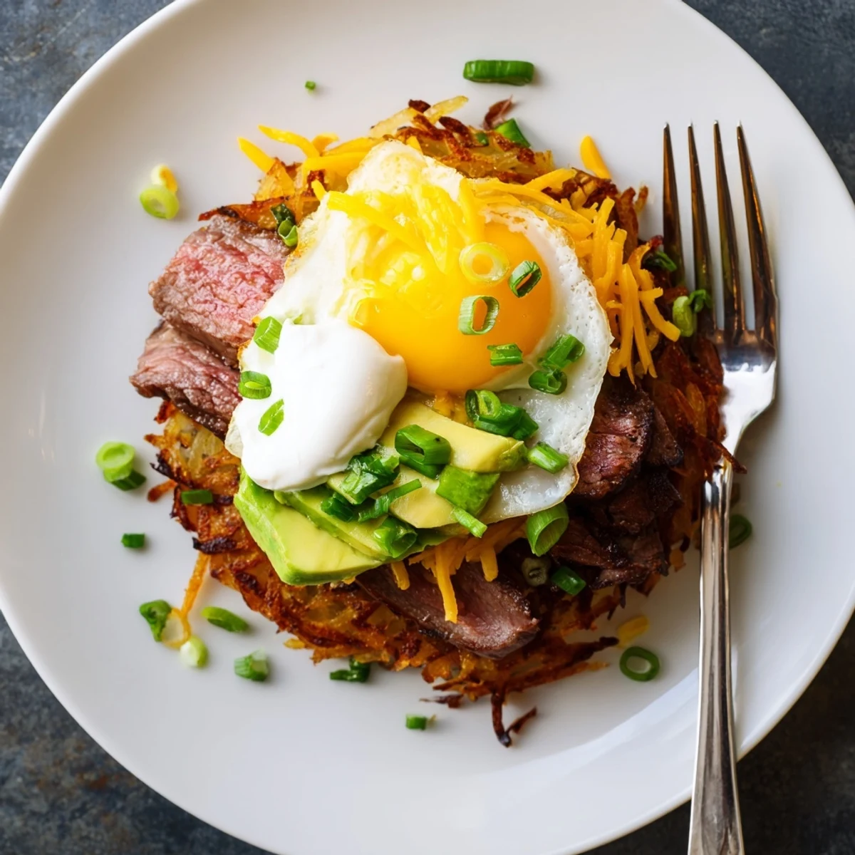 Loaded Steak Egg Hash Brown Stacks with sunny eggs, avocado, and melted cheddar