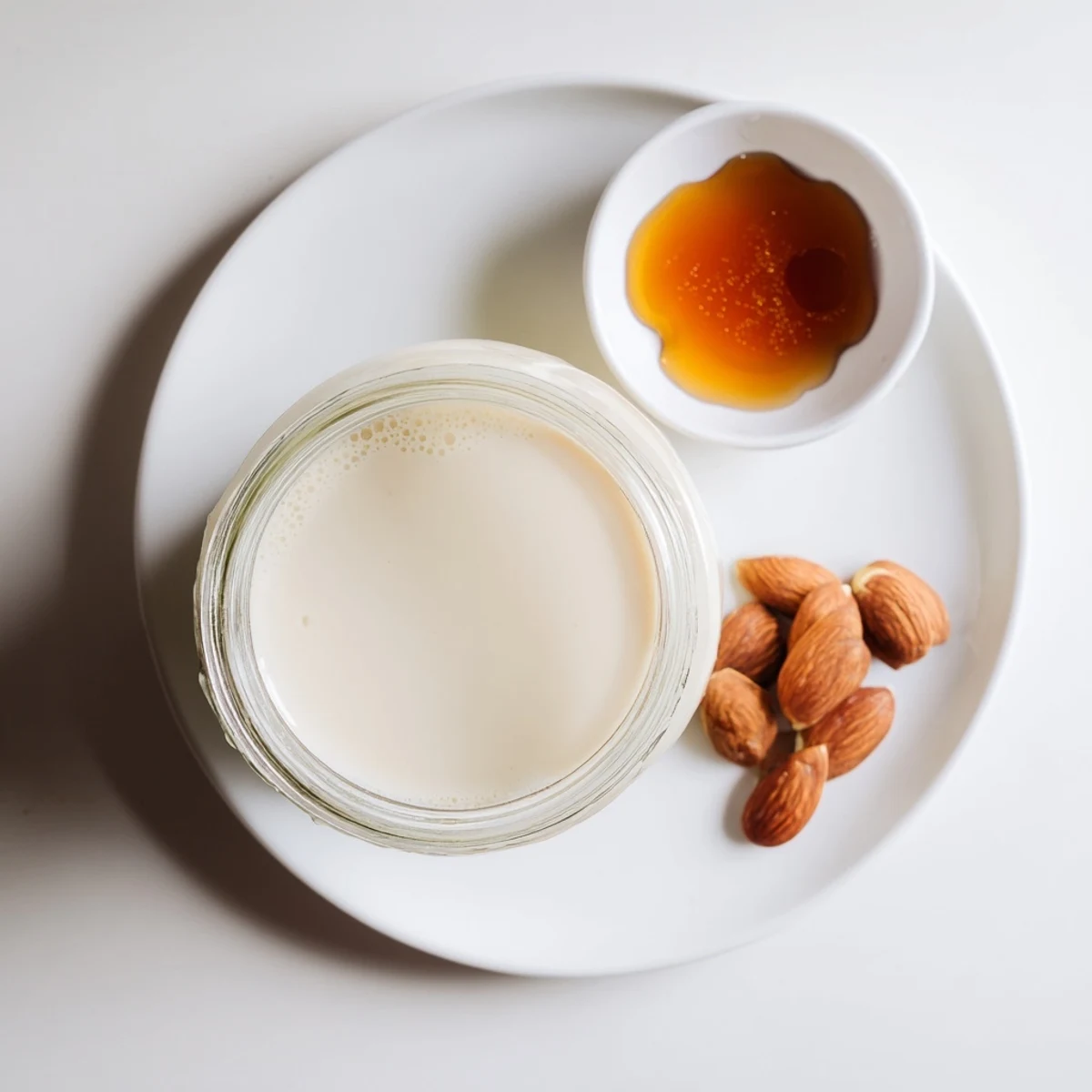 Glass of creamy almond milk resting on wooden table with scattered raw almond pieces
